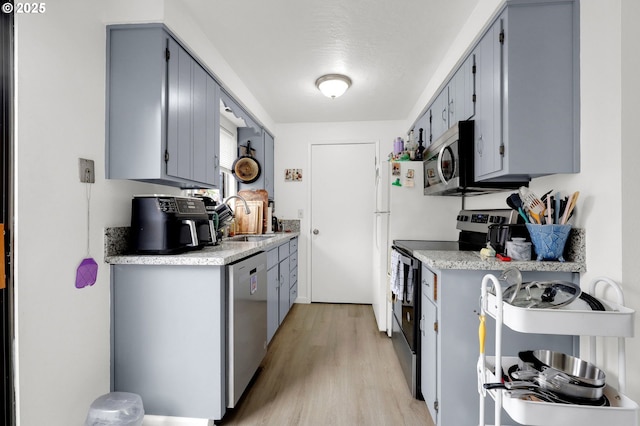 kitchen with appliances with stainless steel finishes, gray cabinets, light countertops, and a sink