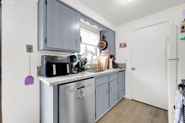 kitchen featuring freestanding refrigerator, light countertops, stainless steel dishwasher, light wood-style floors, and a sink