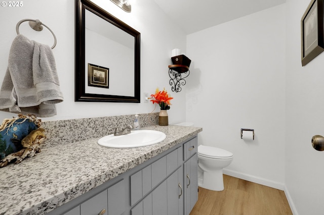 bathroom featuring toilet, baseboards, wood finished floors, and vanity