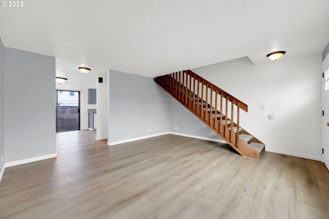 unfurnished living room with light wood-style floors, baseboards, and stairway