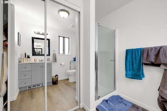 bathroom featuring toilet, wood finished floors, vanity, baseboards, and a stall shower