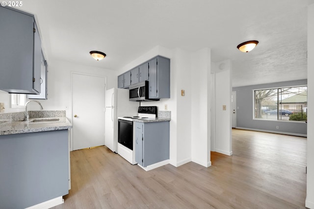 kitchen with range with electric stovetop, a sink, freestanding refrigerator, light wood finished floors, and stainless steel microwave