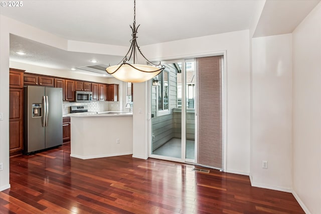 kitchen featuring dark hardwood / wood-style floors, backsplash, stainless steel appliances, and decorative light fixtures