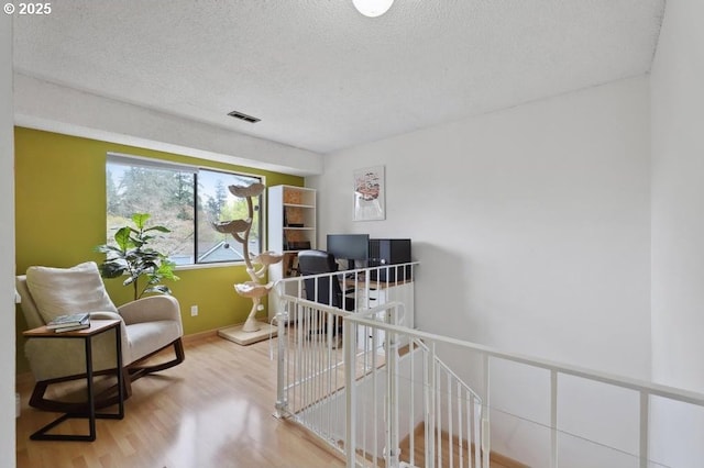 interior space with a textured ceiling, baseboards, wood finished floors, and visible vents
