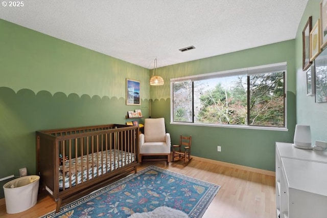 bedroom with a textured ceiling, baseboards, wood finished floors, and visible vents