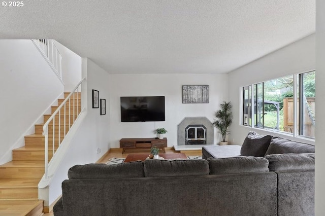 living room featuring stairway, baseboards, a glass covered fireplace, and a textured ceiling