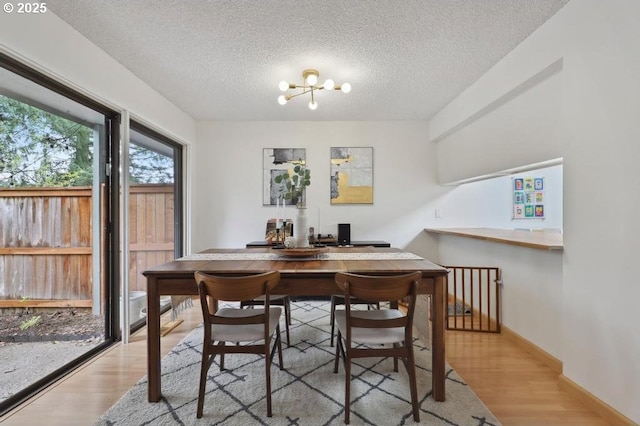 dining space featuring an inviting chandelier, baseboards, a textured ceiling, and wood finished floors
