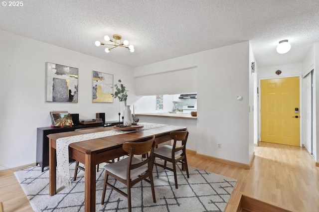 dining space featuring a textured ceiling, a chandelier, baseboards, and light wood-type flooring