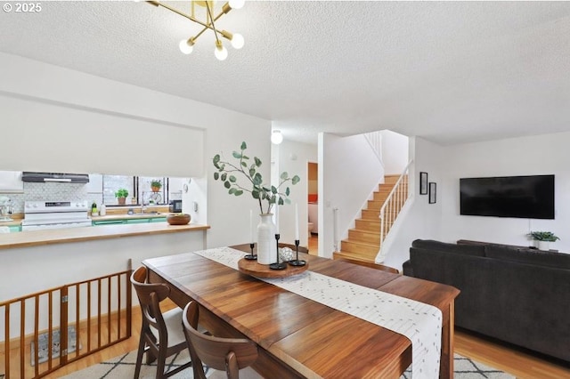dining area featuring stairs, a textured ceiling, a notable chandelier, and light wood-style flooring