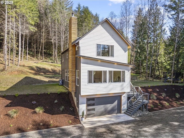 view of front of home featuring driveway, an attached garage, central AC, a chimney, and a trampoline