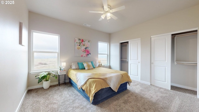 carpeted bedroom with a ceiling fan, visible vents, baseboards, and two closets