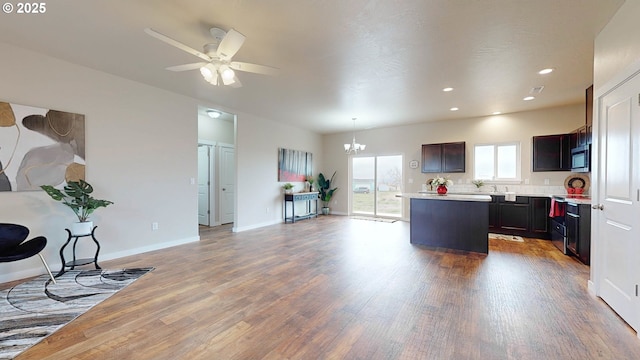 kitchen featuring ceiling fan with notable chandelier, pendant lighting, hardwood / wood-style floors, a center island, and dark brown cabinets