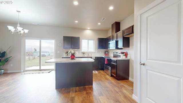 kitchen with pendant lighting, appliances with stainless steel finishes, a center island, an inviting chandelier, and light wood-type flooring