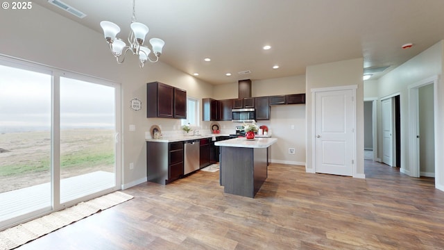 kitchen with appliances with stainless steel finishes, a kitchen island, dark brown cabinets, a chandelier, and pendant lighting