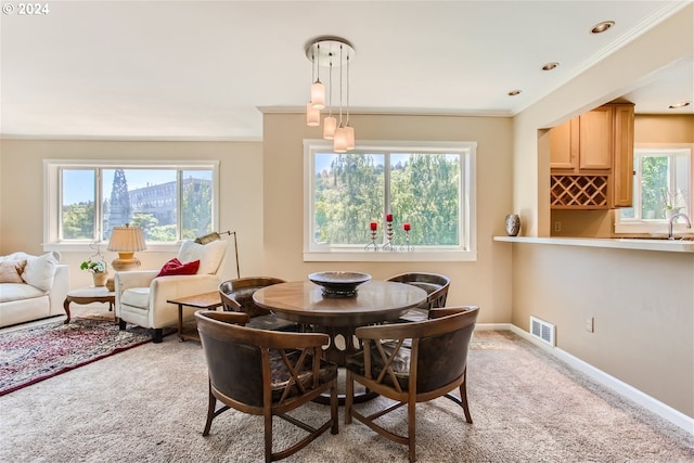 dining space featuring light colored carpet, ornamental molding, sink, and a wealth of natural light