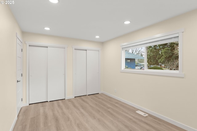 unfurnished bedroom with recessed lighting, visible vents, baseboards, light wood finished floors, and two closets