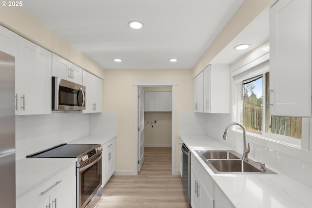 kitchen with white cabinets, appliances with stainless steel finishes, light stone countertops, light wood-type flooring, and a sink