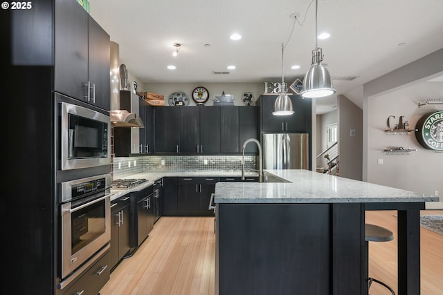 10155 SW Morrison St, Portland, OR 97225 - kitchen featuring stainless steel appliances, light wood-type flooring, decorative backsplash, a kitchen island with sink, and a kitchen bar