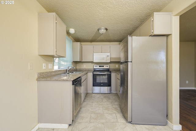 kitchen with sink, a textured ceiling, light tile patterned floors, stainless steel appliances, and white cabinets