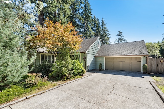 view of front of house with roof with shingles, driveway, an attached garage, and fence