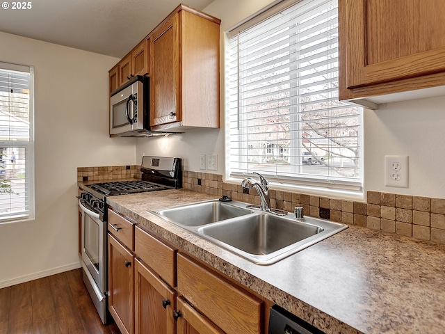 kitchen featuring brown cabinetry, baseboards, a sink, dark wood-type flooring, and appliances with stainless steel finishes