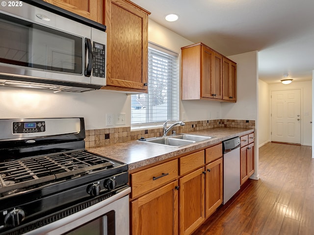 kitchen featuring brown cabinetry, baseboards, appliances with stainless steel finishes, dark wood-style floors, and a sink