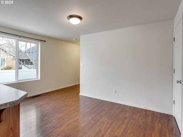 spare room with dark wood-type flooring, baseboards, visible vents, and a textured ceiling