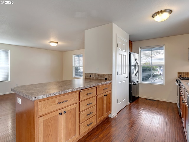 kitchen with a peninsula, dark wood-style floors, tasteful backsplash, and stainless steel appliances