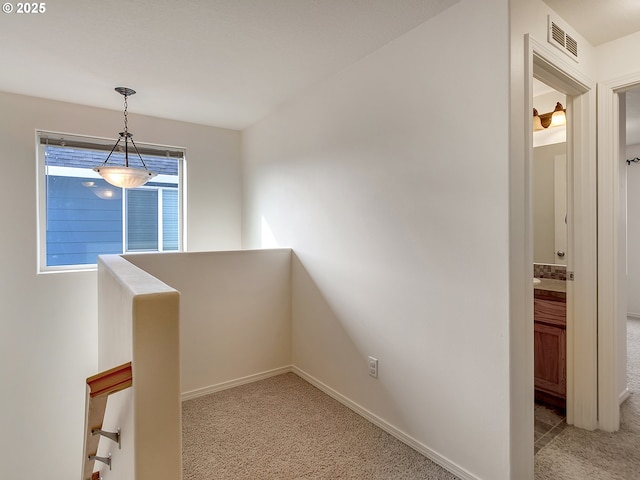 hall featuring baseboards, visible vents, an upstairs landing, and carpet floors