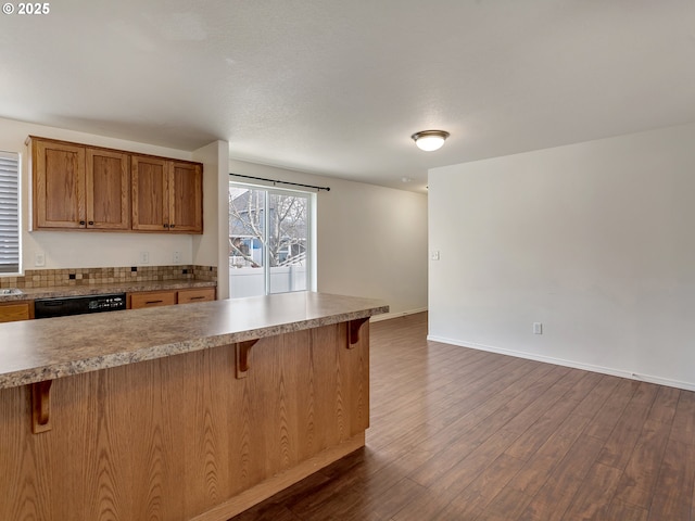 kitchen featuring a breakfast bar area, brown cabinetry, baseboards, dark wood finished floors, and black dishwasher