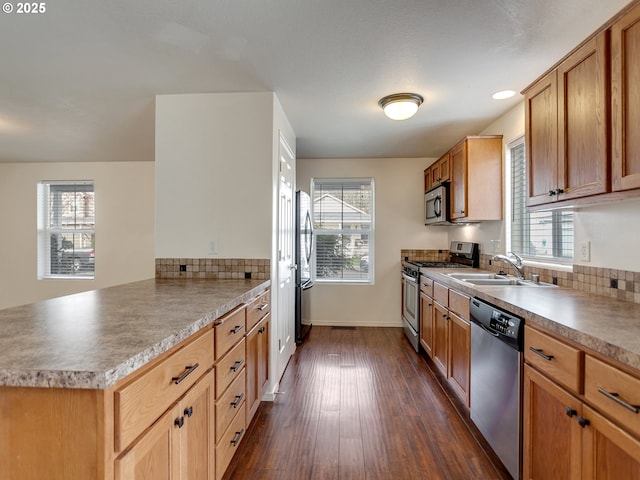 kitchen with a sink, dark wood finished floors, stainless steel appliances, a peninsula, and baseboards