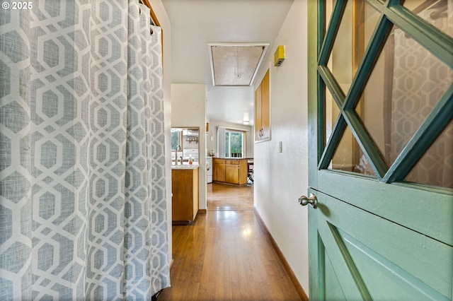 hall featuring a sink, baseboards, attic access, and wood finished floors