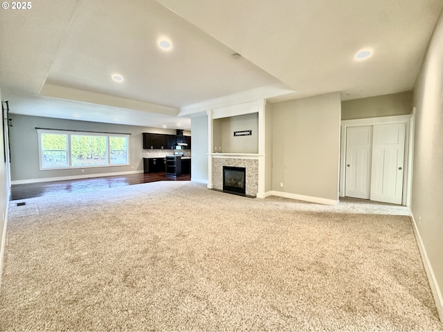 unfurnished living room with a raised ceiling, carpet flooring, and a tiled fireplace