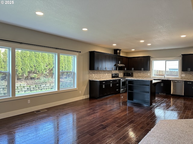 kitchen with light stone countertops, dark hardwood / wood-style floors, stainless steel appliances, a kitchen island, and backsplash