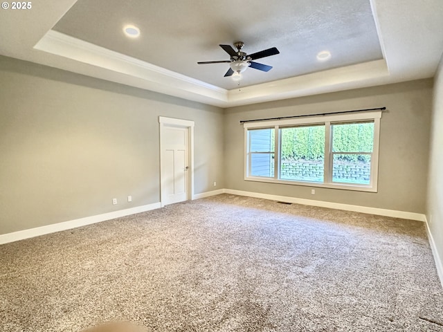 empty room featuring a raised ceiling, carpet floors, and ceiling fan