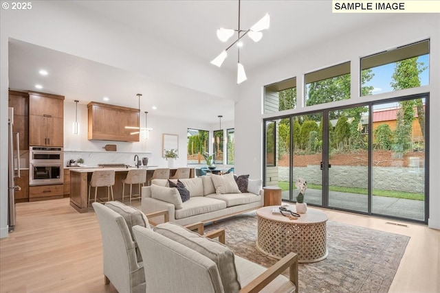 living room with a chandelier, recessed lighting, light wood-style floors, and a high ceiling