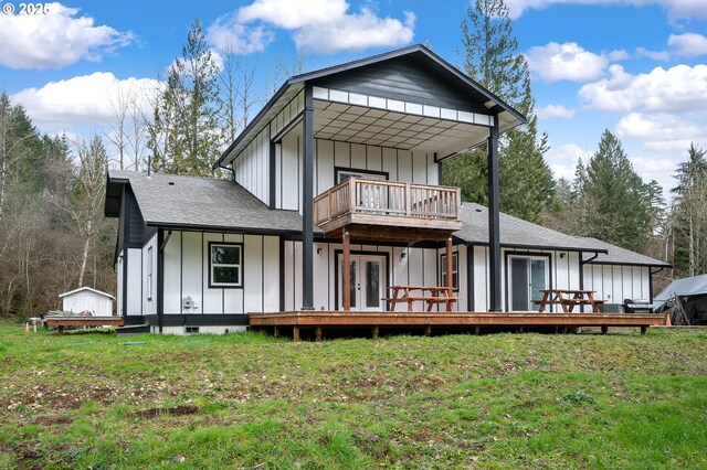 back of house featuring board and batten siding, a lawn, a detached carport, a balcony, and french doors