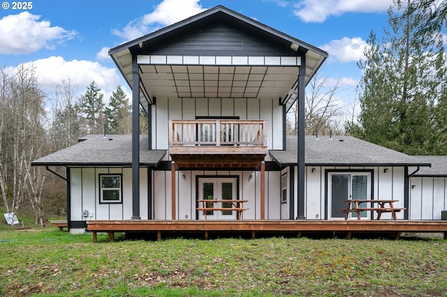 rear view of house with board and batten siding, roof with shingles, a lawn, and a balcony