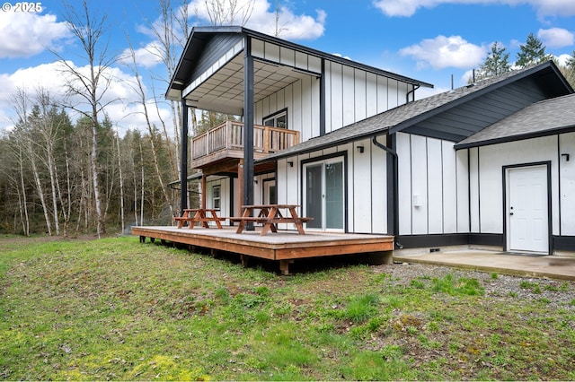 back of property with board and batten siding, a wooden deck, a yard, and a balcony