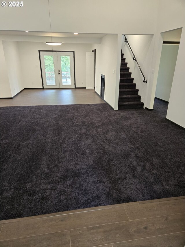 unfurnished living room featuring carpet floors, french doors, wood finished floors, and stairway