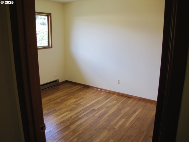 spare room featuring wood-type flooring and a baseboard heating unit