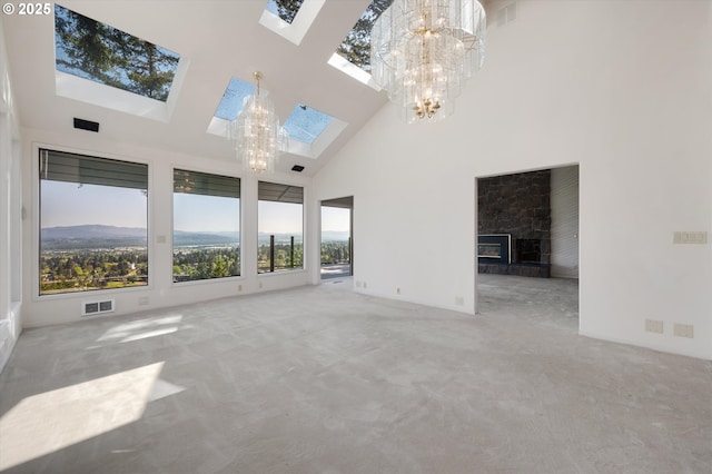 unfurnished living room featuring a skylight, a chandelier, a high ceiling, carpet, and a fireplace with raised hearth