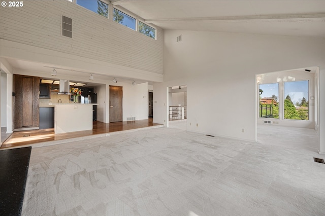 unfurnished living room featuring high vaulted ceiling, light carpet, and baseboards