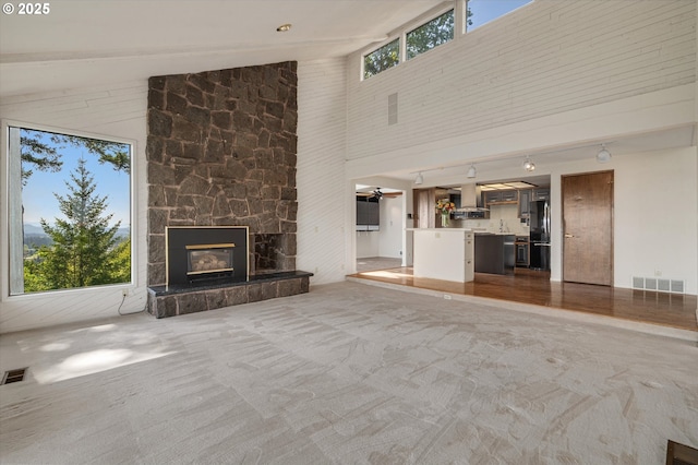unfurnished living room featuring high vaulted ceiling, carpet flooring, a fireplace, and a ceiling fan