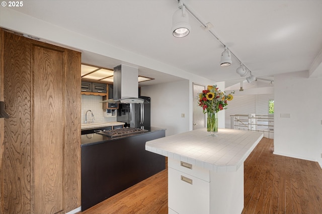 kitchen with island exhaust hood, tile countertops, stainless steel gas stovetop, light wood-style flooring, and decorative backsplash