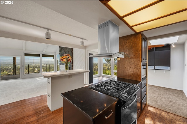 kitchen with black range with gas cooktop, island exhaust hood, hardwood / wood-style flooring, tile countertops, and track lighting
