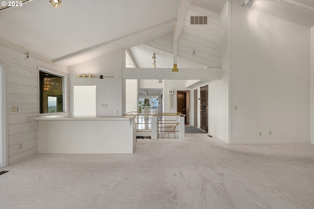 unfurnished living room with high vaulted ceiling, beam ceiling, and carpet