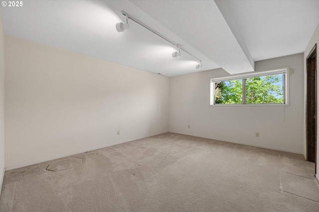 spare room featuring light carpet, track lighting, and baseboards