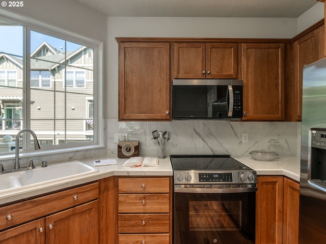 11656 SW Auklet Loop, Beaverton, OR 97007 - kitchen with appliances with stainless steel finishes, light countertops, brown cabinetry, decorative backsplash, and healthy amount of natural light