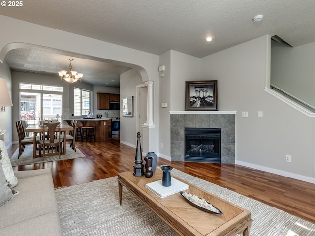 11656 SW Auklet Loop, Beaverton, OR 97007 - living room featuring dark wood-type flooring, a tiled fireplace, a textured ceiling, a chandelier, and decorative columns